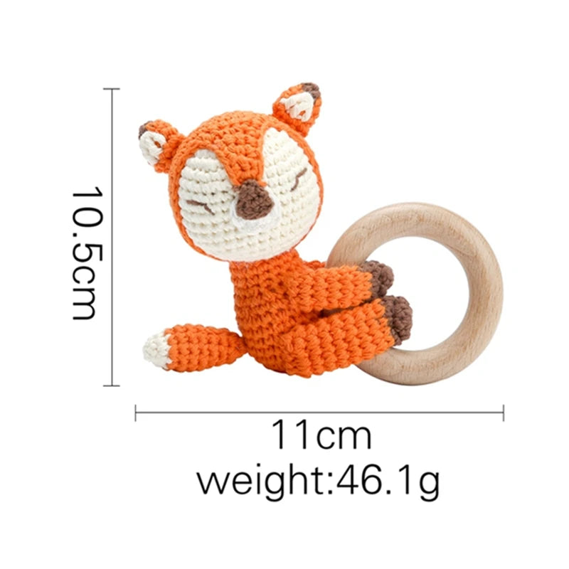 Crocheted orange fox teether with a wooden ring. The fox is 10.5 cm tall, 11 cm wide, and weighs 46.1 g. Features include a white face, closed eyes, and brown details.