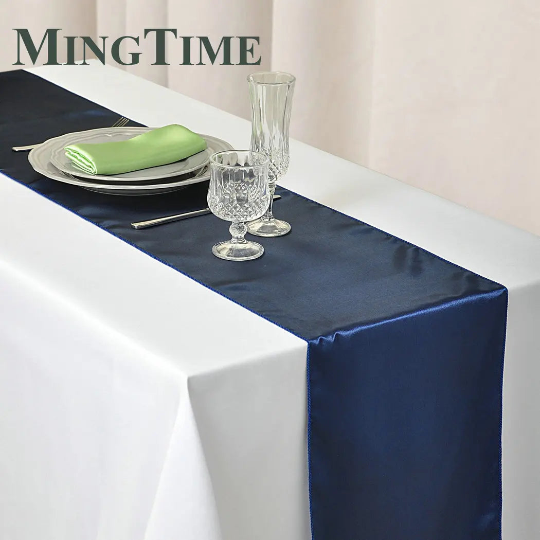 Elegant table setting with a white tablecloth and blue satin runner. Features glassware, a plate with a green napkin, silverware, and the text "MingTime" in the corner.