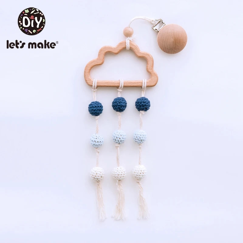 Wooden cloud-shaped baby mobile with crocheted balls in shades of blue and white, hanging from three strings. A wooden clip is attached for securing.