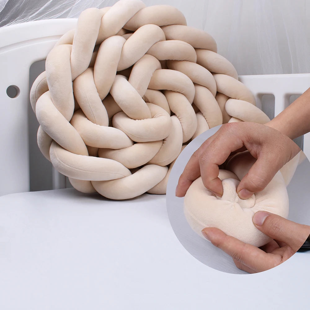 Beige braided cushion on a white surface, with a close-up of hands pressing into its soft, plush fabric, demonstrating its softness and texture.