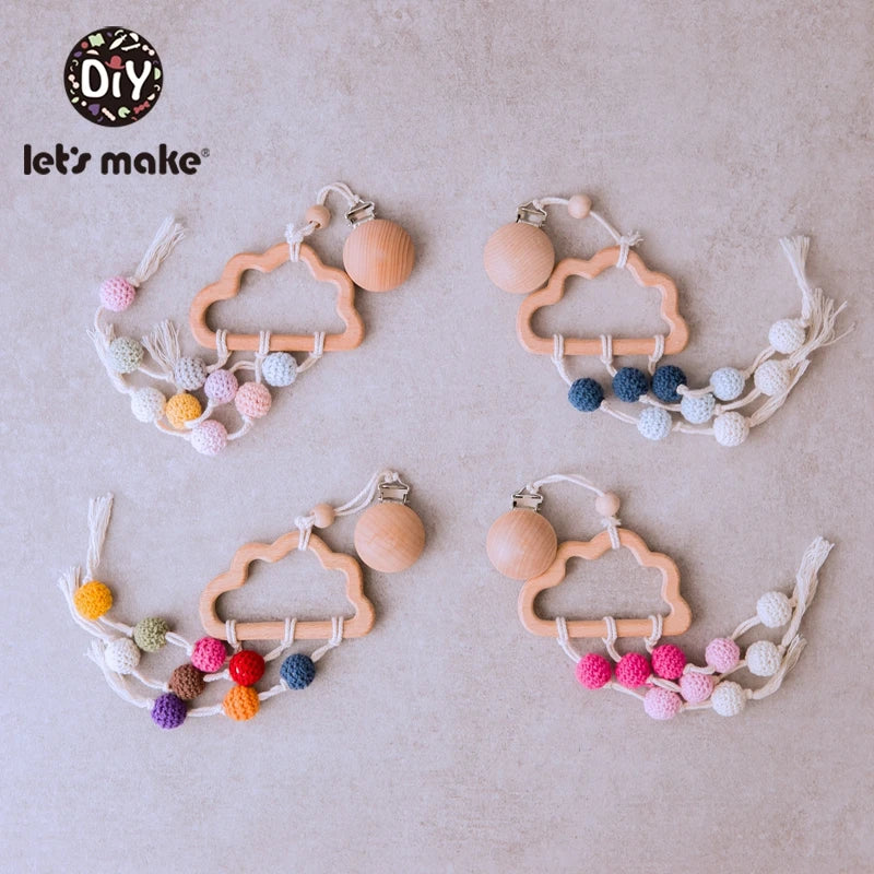 Four cloud-shaped wooden baby pacifier clips with colorful crochet beads are arranged on a beige background. Each clip features different bead color combinations: pastel, blue, multicolor, and pink.