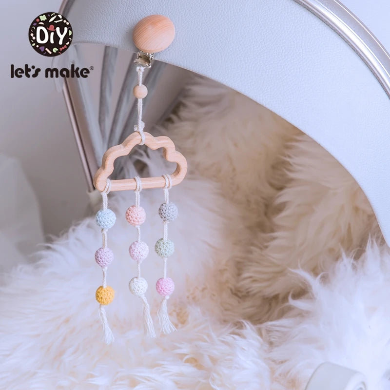 Wooden cloud hanger with colorful crocheted balls hangs on a white surface. Background features a fluffy, cream textured fabric. DIY logo in the top left corner.