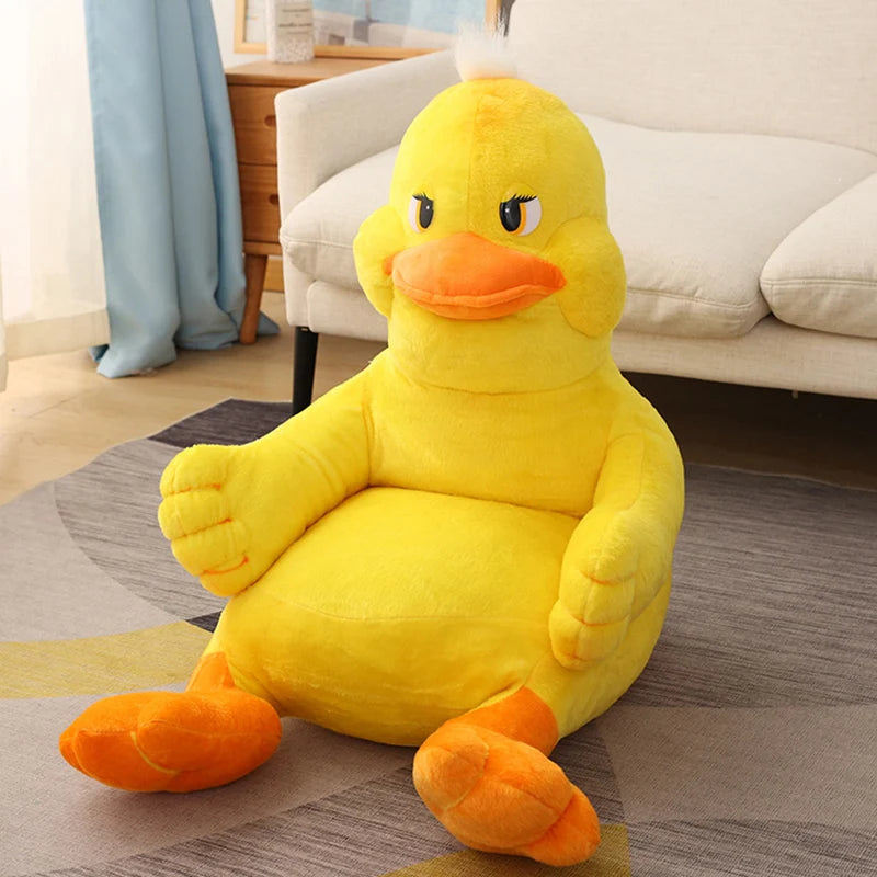 A plush, oversized yellow duck chair with a playful expression sits on a gray and yellow rug in a cozy room. The chair has orange feet and beak, complementing the soft decor.
