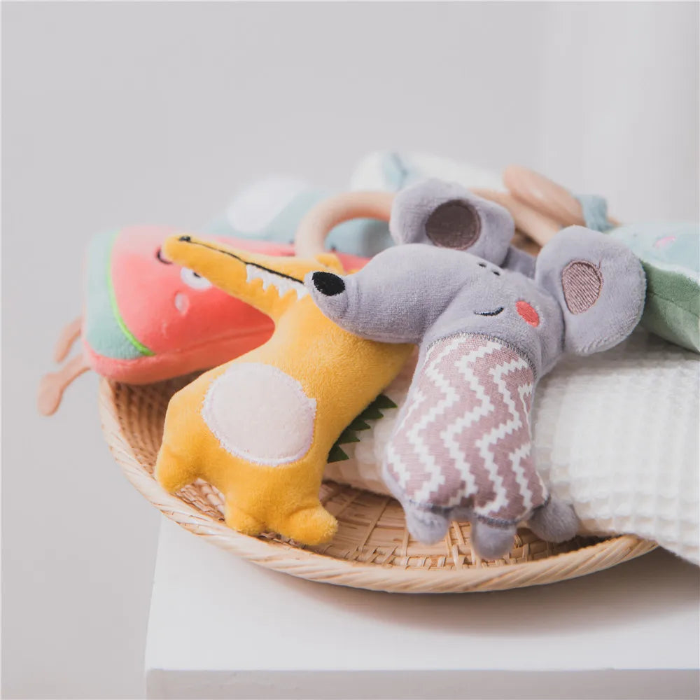 A wicker basket holds colorful plush toys, including a yellow animal and a gray mouse with zigzag details, resting on a white textured cloth.