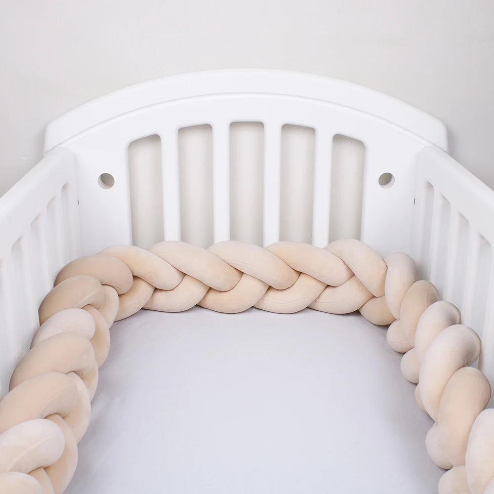 White crib with a braided beige crib bumper. The bumper lines the interior, providing cushioning and safety for the baby.