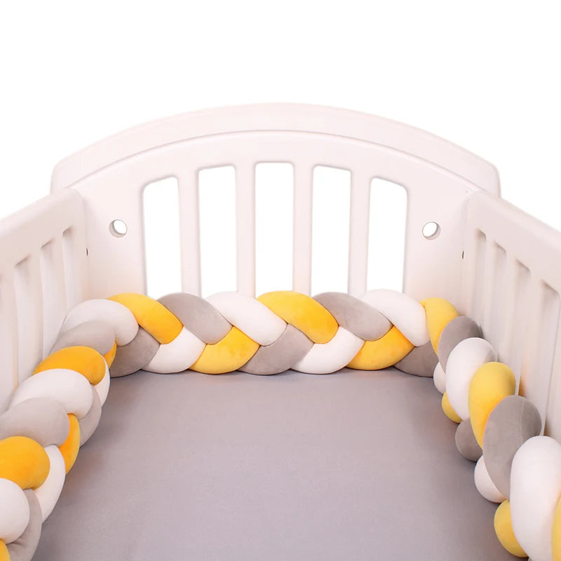 White crib with a twisted, plush bumper in yellow, gray, and white hues surrounding the inside of the crib. The mattress is covered with a plain gray sheet.