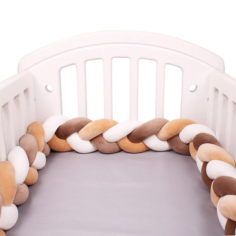 White crib with a braided bumper in shades of brown, beige, and white. The mattress is gray, and the bumper adds a soft, decorative touch to the crib's interior.