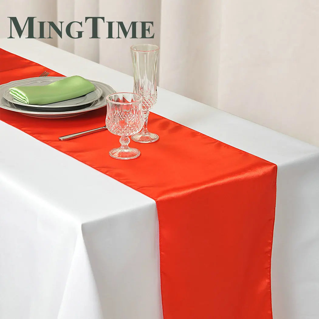 Elegant table setting with a red satin table runner over a white cloth. Includes crystal glasses, plates, a green napkin, and utensils, with "MingTime" text in the corner.
