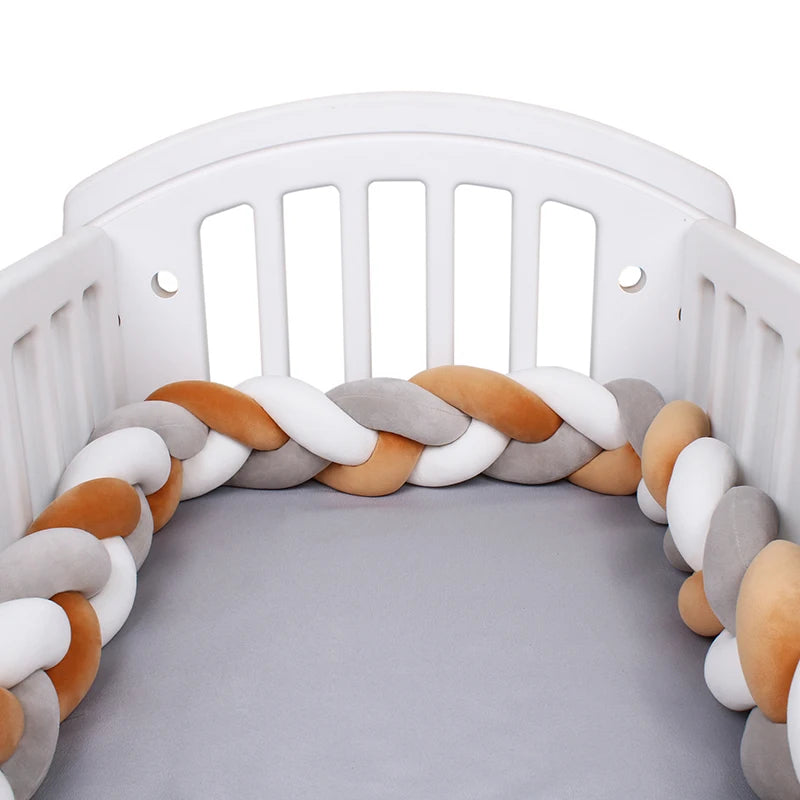 White crib with a soft, braided bumper in gray, white, and peach colors surrounding the mattress, providing a cozy and safe environment for a baby.