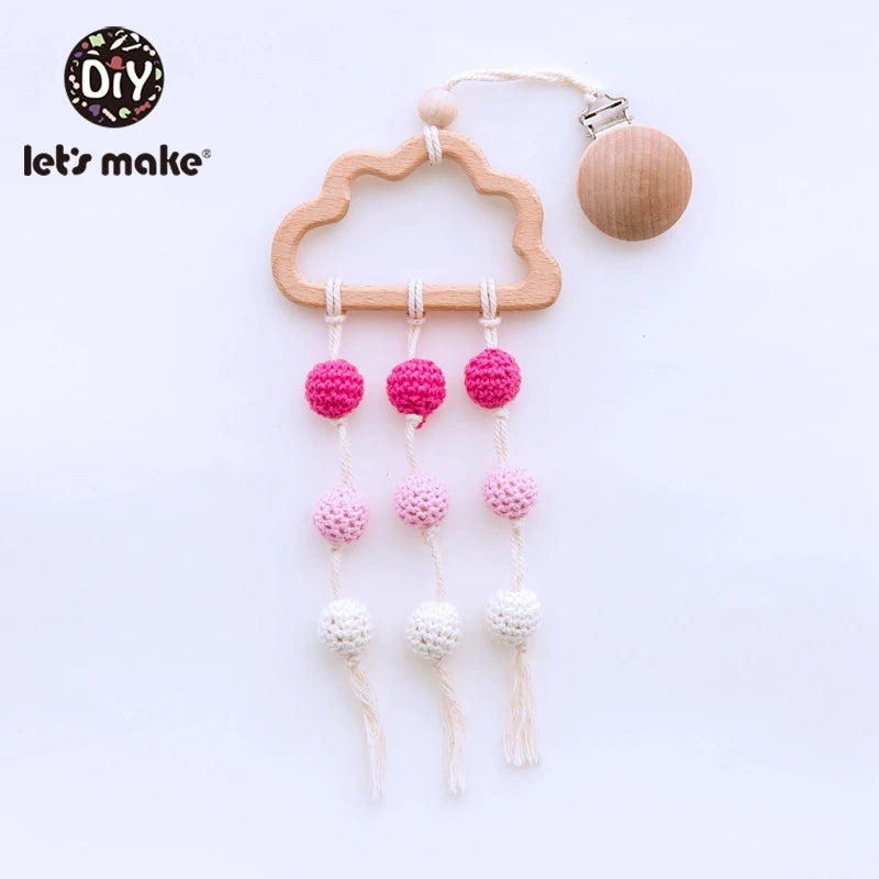Wooden cloud-shaped teether with multicolored crochet beads hanging on strings. The design includes pink and white beads and a wooden clip for attachment.