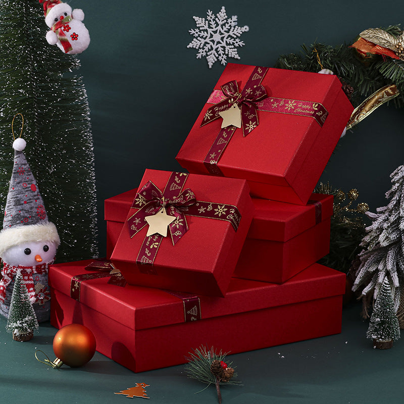 A stack of red gift boxes with gold star ornaments and bows, surrounded by festive decorations including a snowman, pine branches, a snowflake, and a Christmas ornament.