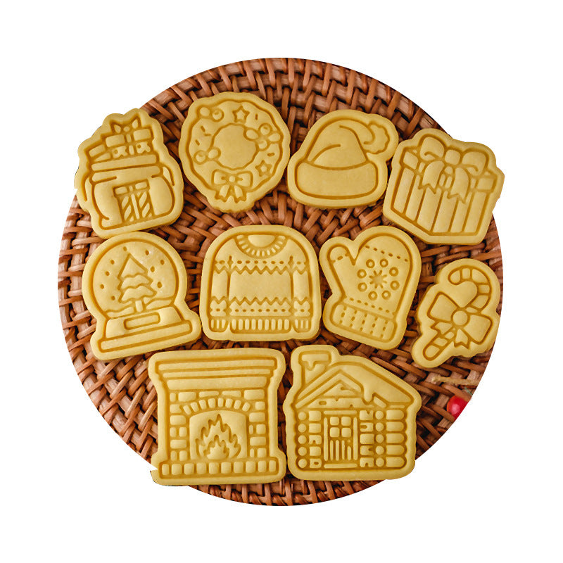 A round wicker tray holds ten festive cookies shaped like a wreath, gifts, mitten, candy cane, sweater, fireplace, log cabin, Santa hat, and snow globe.