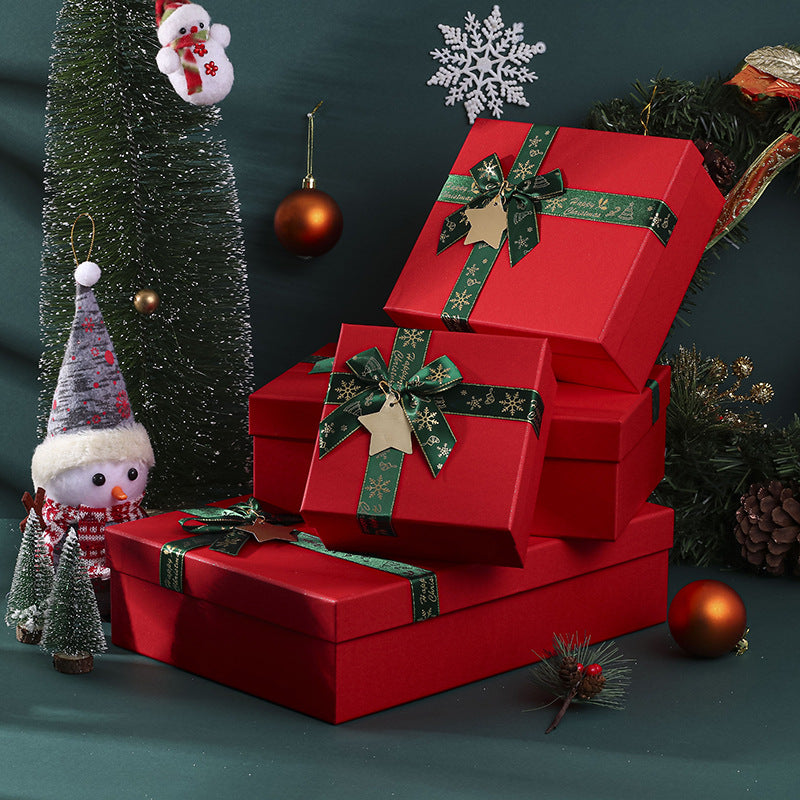 A stack of red gift boxes with green ribbons, surrounded by a snowman figurine, Christmas tree, ornaments, and a snowflake decoration on a festive background.