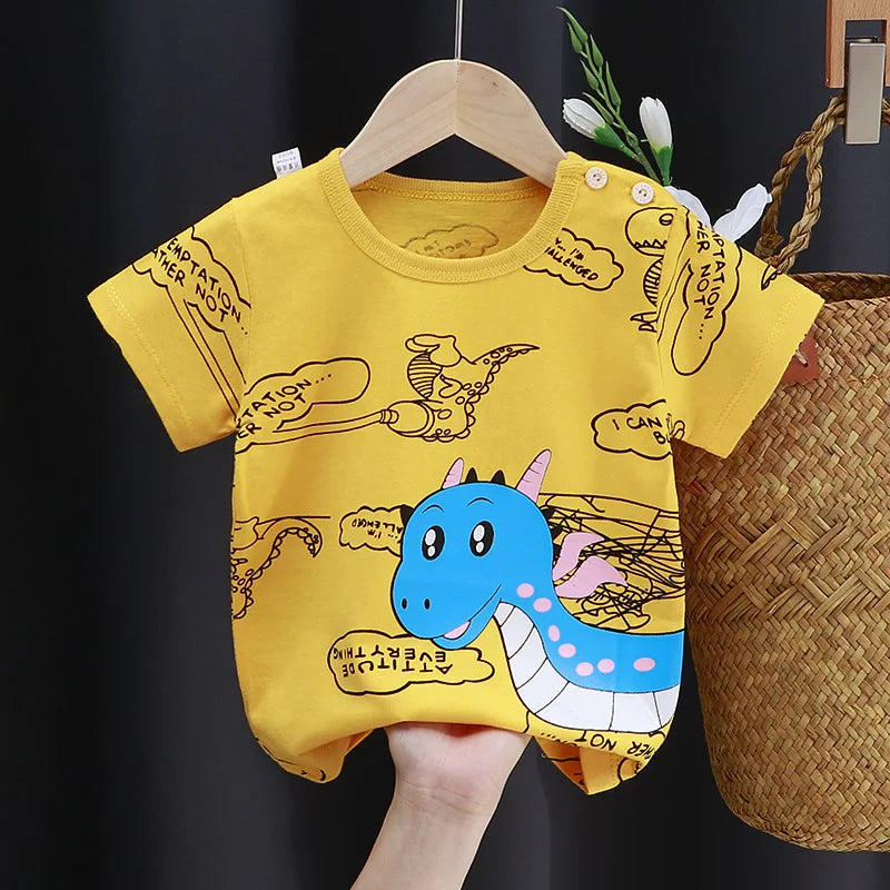 Yellow baby romper with blue cartoon dragon and playful sketches. Features short sleeves and shoulder buttons. Hangs on a wooden hanger beside a woven basket and green plant.