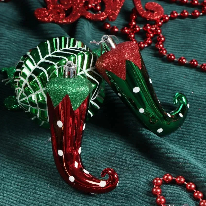 Two elf shoe-shaped Christmas ornaments, one red and green with glitter, the other green with white polka dots, lie on a teal fabric near a green-striped ball and red bead garland.