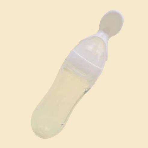 Transparent baby feeding bottle with a white spoon attached at the top, designed for easy dispensing of food or liquid. Set against a plain beige background.