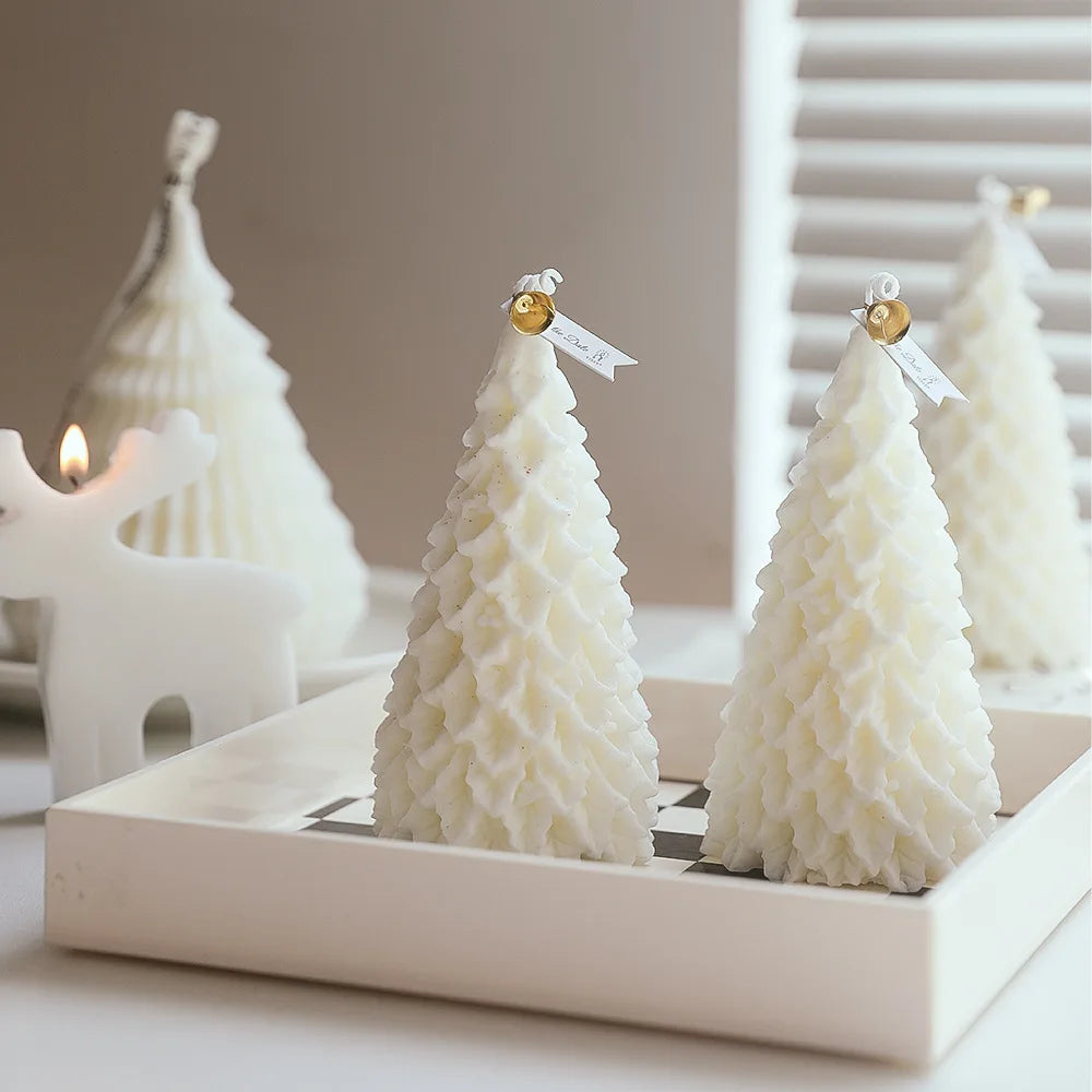 White, tree-shaped candles with decorative tags are displayed on a square tray. A lit reindeer-shaped candle is in the background, creating a cozy, festive atmosphere.