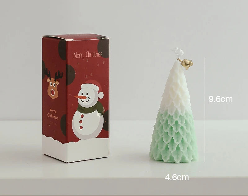 Christmas-themed candle shaped like a tree with white and green layers, adorned with a small bell. Dimensions are 9.6cm tall and 4.6cm wide. Box features festive snowman design.