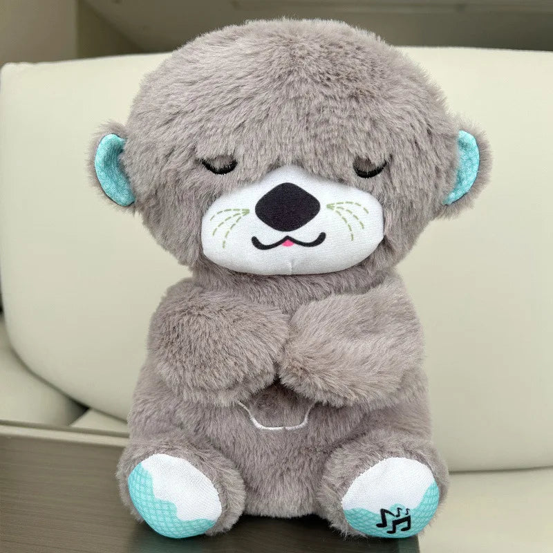 A soft, gray plush otter with closed eyes and a serene expression, featuring teal inner ears and paws, sits against a light background.