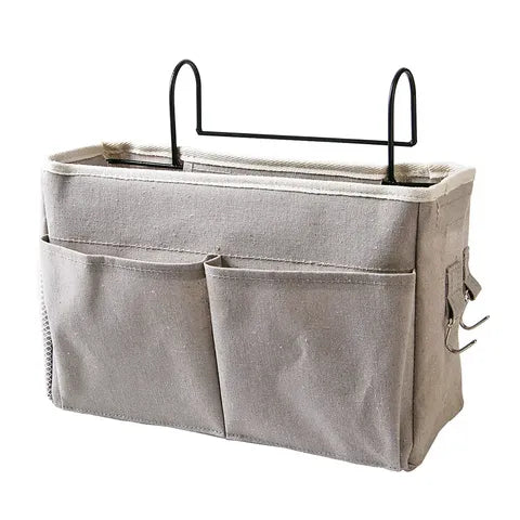 Beige fabric hanging organizer with multiple pockets and two metal hooks for easy attachment. Ideal for storage on beds or sofas, keeping essentials within reach.