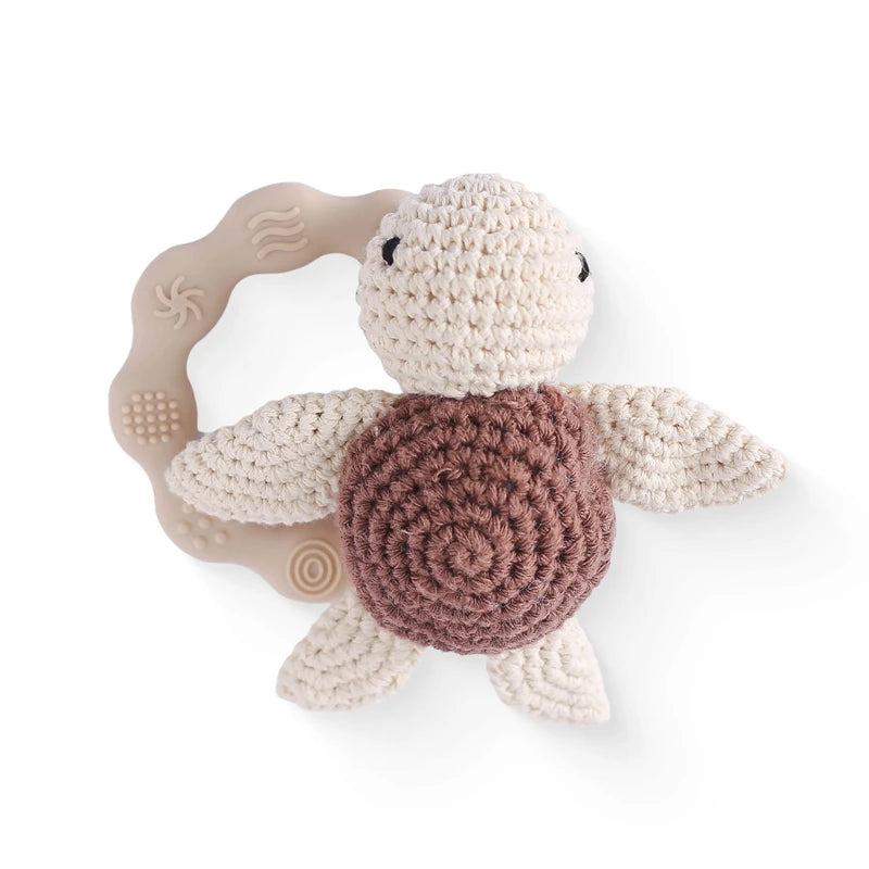 Crocheted turtle toy with a soft, textured beige shell and off-white limbs, attached to a beige silicone teething ring with various patterns, suitable for babies.