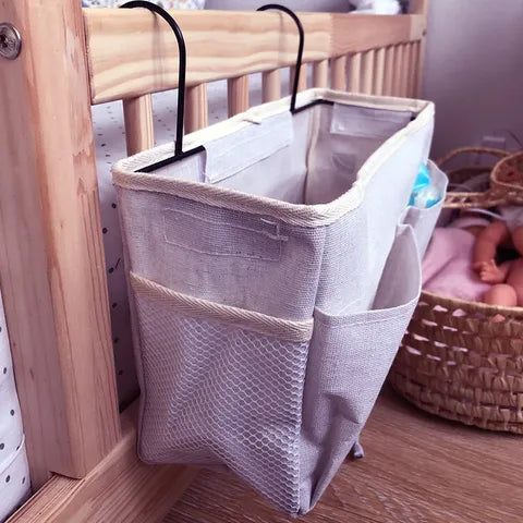 Hanging fabric organizer attached to a crib, featuring multiple pockets for storage. A baby doll in a basket is visible on the floor in the background.