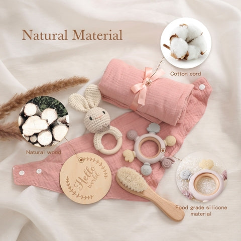 Baby items made from natural materials displayed on a cloth: wooden toy, cotton cord, silicone teether, brush, and cloth roll. Circular insets highlighting wood and cotton details.