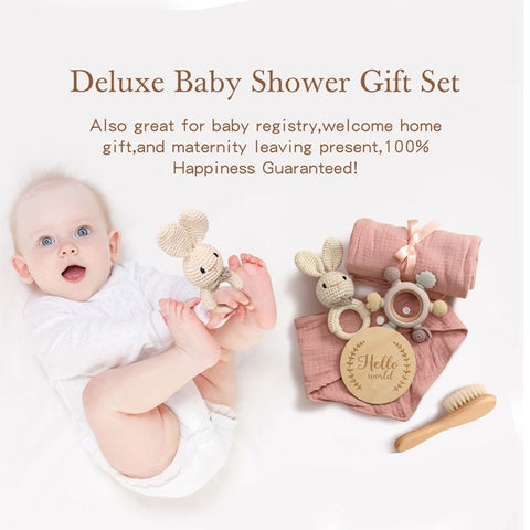 A smiling baby lies on a white background beside a deluxe baby shower gift set, including a pink blanket, plush toys, a wooden brush, and a “Hello World” sign. Text highlights gift uses.