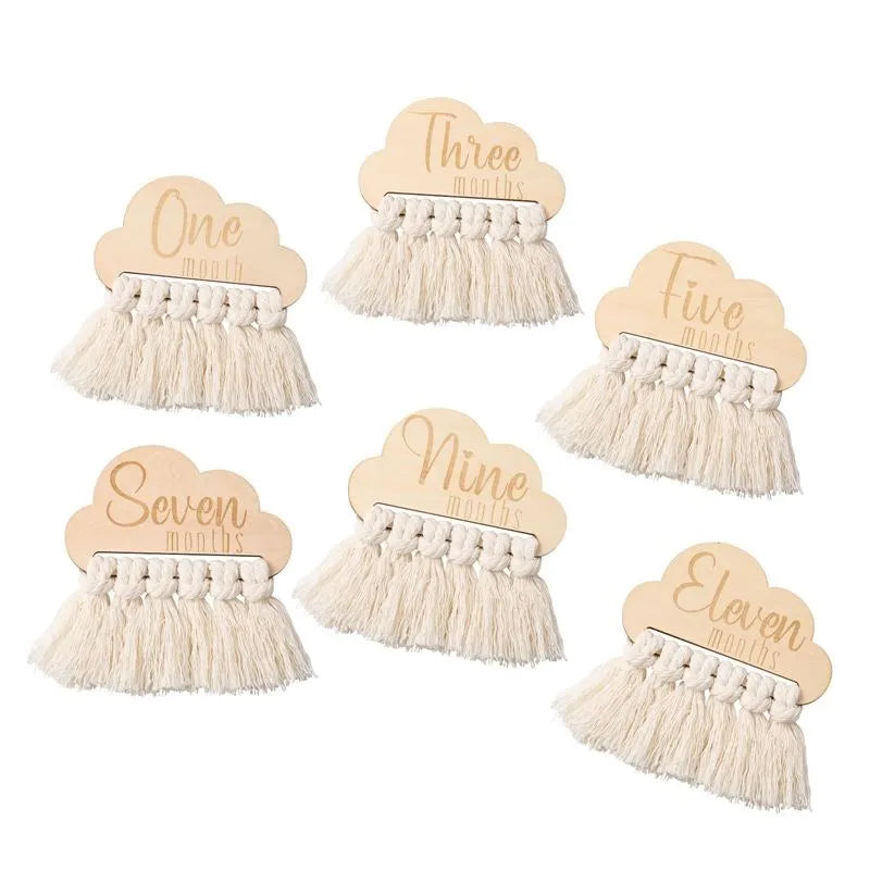 Wooden cloud-shaped milestone markers with tassels, each labeled with different months: One, Three, Five, Seven, Nine, and Eleven, arranged in a scattered pattern.