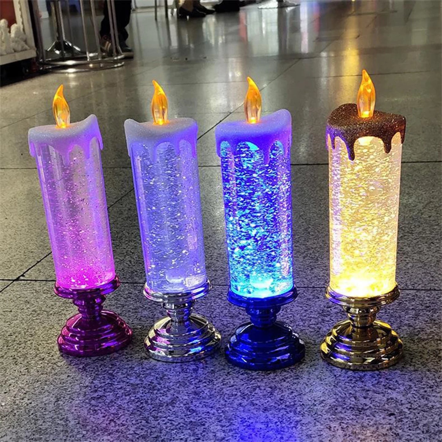 Four decorative candles with colored LED lights and glitter inside, each on a shiny base. They glow in pink, white, blue, and yellow with realistic flame tips.