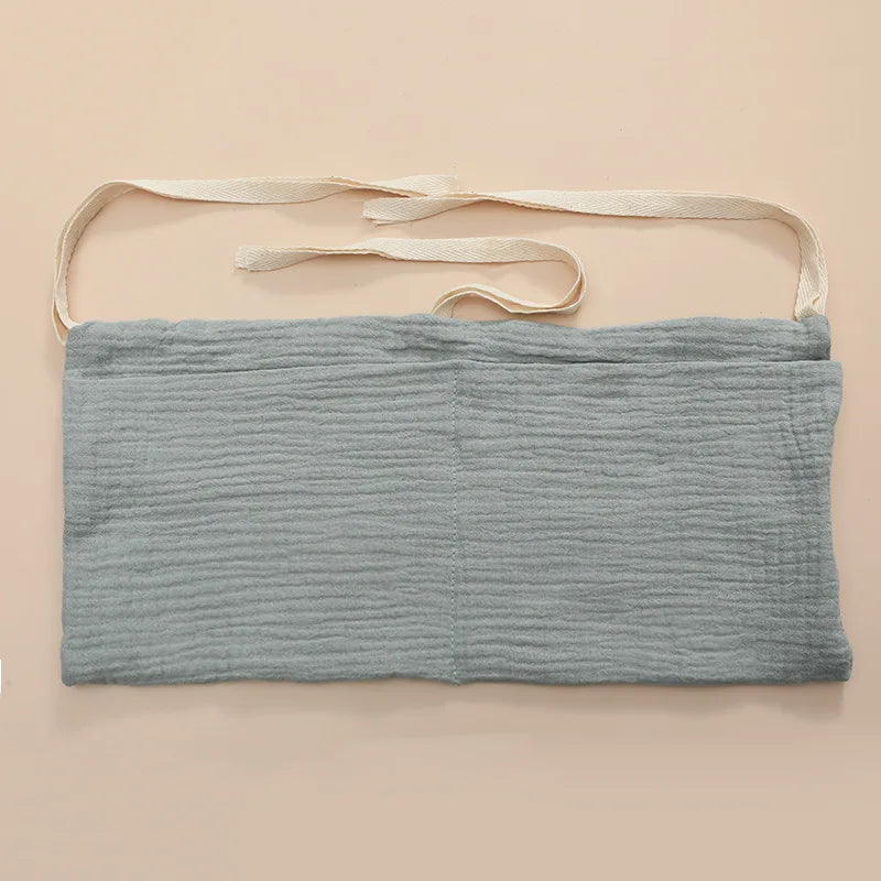 A light blue, textured cotton fabric apron with cream-colored ties, displayed flat on a beige surface.