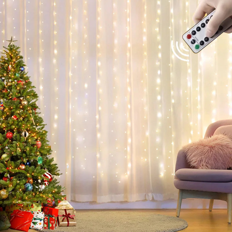A decorated Christmas tree with gifts beneath stands beside a cozy pink chair. Warm string lights hang in the background, controlled by a remote held by a hand.