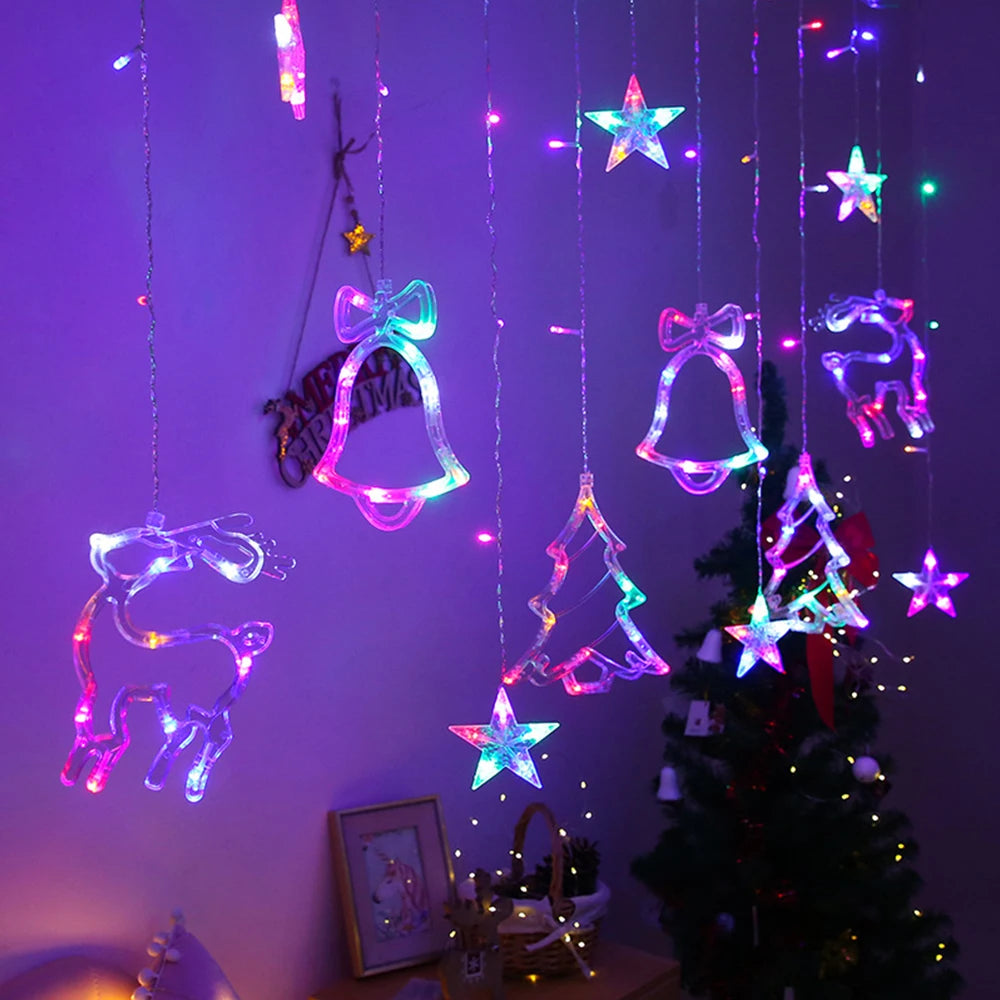 Hanging Christmas decorations with LED lights, including stars, bells, trees, and reindeer, glow in various colors against a dark room, with a decorated Christmas tree in the background.