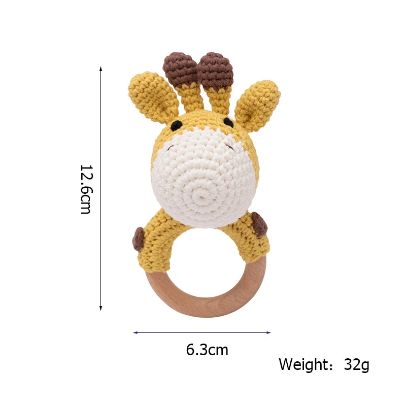Crocheted giraffe baby rattle with a wooden ring. Dimensions: 12.6cm tall, 6.3cm wide. Weight: 32g. Features a yellow and white crocheted design with small brown details.