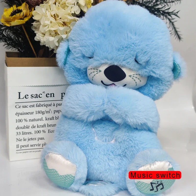 A fluffy blue teddy bear with eyes closed sits in front of a flower arrangement. The bear has a music switch button on its foot highlighted in red text.