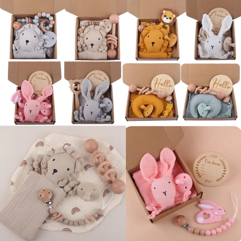 Collection of baby gift sets in brown boxes, featuring plush animal toys, teethers, and wooden "Hello World" signs. Includes pink, grey, mustard, and teal variations.