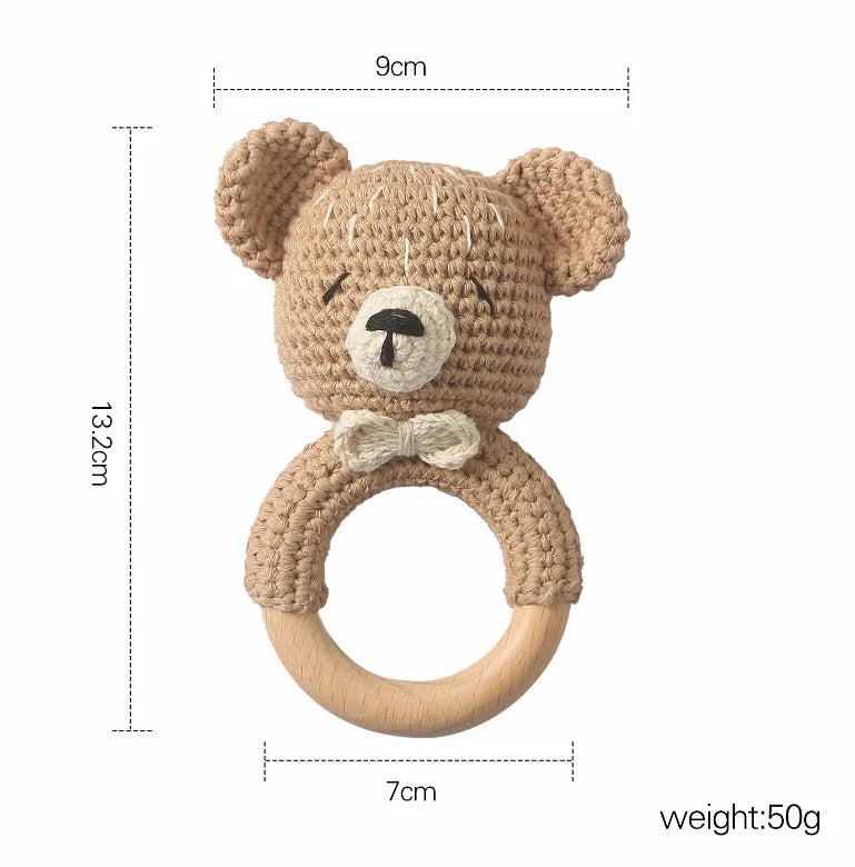 Crocheted bear-shaped baby rattle with a wooden ring, measuring 13.2cm in height and 9cm in width. It features a small bow tie and weighs 50g.