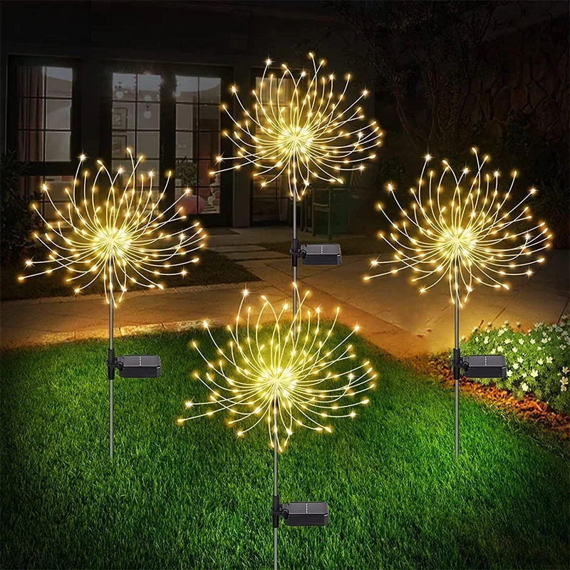 Four solar-powered dandelion-shaped LED lights glowing warmly on a grassy lawn near a house at night, creating a festive and welcoming outdoor atmosphere.