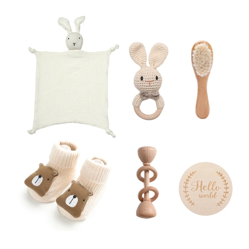 Collection of baby items: a white bunny security blanket, a crocheted bunny rattle, a wooden hairbrush, bear face socks, a wooden teether, and a "Hello world" wooden plaque.