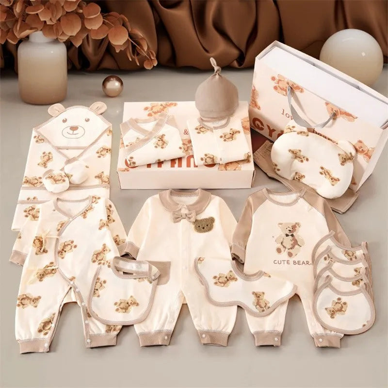 Baby clothing set with bear patterns, featuring onesies, bibs, a hat, and mittens in beige and cream tones. Packaged in a gift box with a matching gift bag, against a soft backdrop.