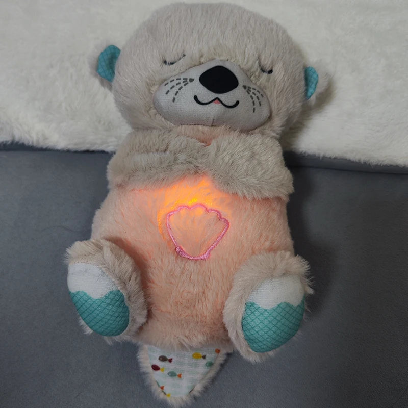 A plush toy otter with a smiling face lies on a soft surface. Its belly glows warmly, illuminating a pink shell design. The otter features teal accents on its ears and feet.