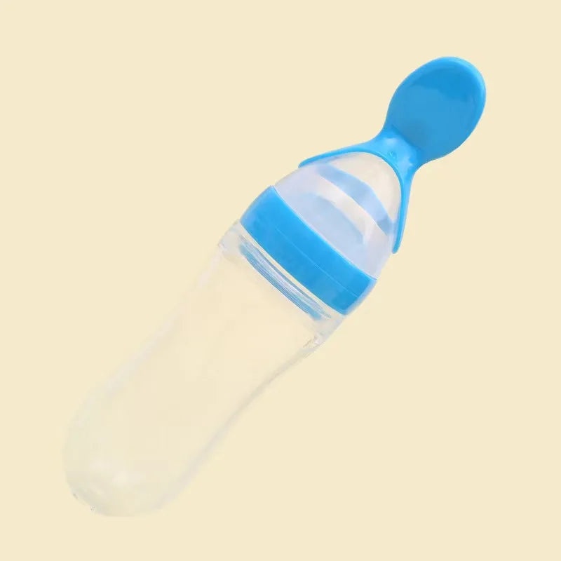 A transparent baby bottle with a light blue cap and built-in spoon, set against a cream background.