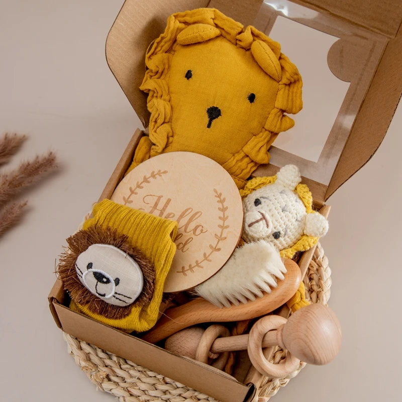 A gift basket featuring a mustard-colored lion plush, a round wooden plaque with "Hello World," a woven lion toy, a baby brush, wooden teethers, and lion-themed baby socks.