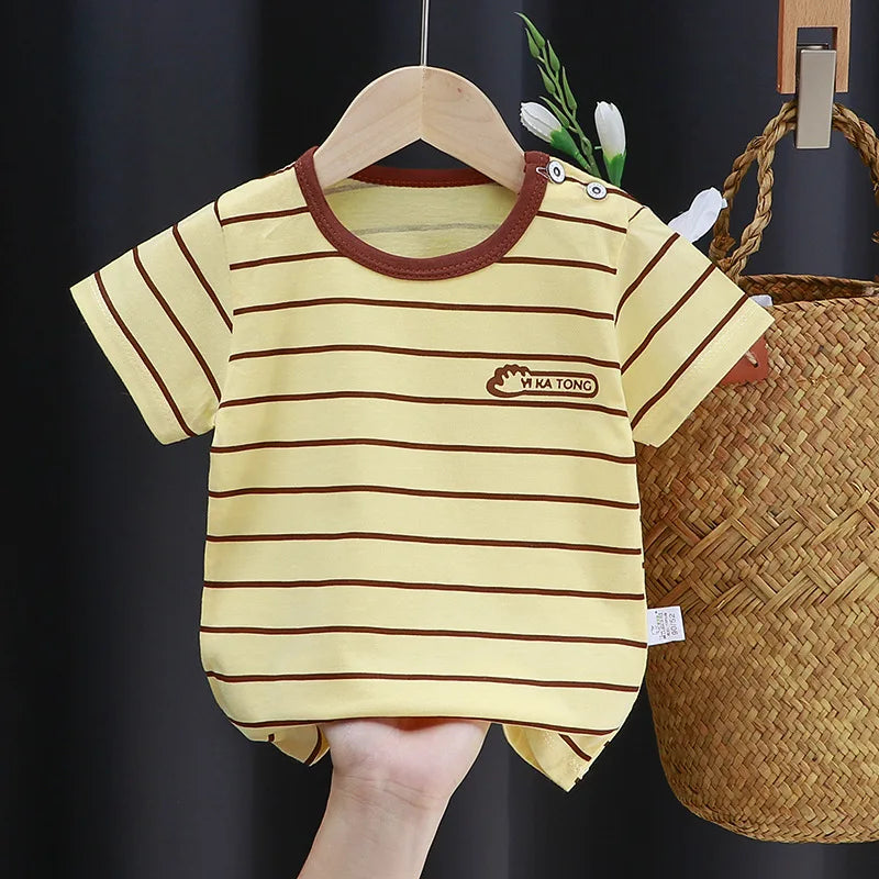 Yellow baby romper with brown stripes, a brown collar, and the text "KA TONG" on the chest. It's displayed on a hanger with a wicker basket in the background.