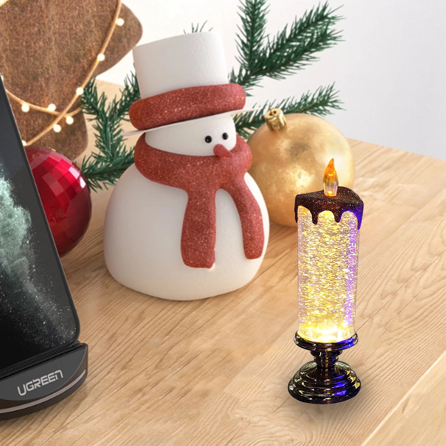 Festive snowman decoration with red scarf beside a glittery LED candle and Christmas ornaments on a wooden table.