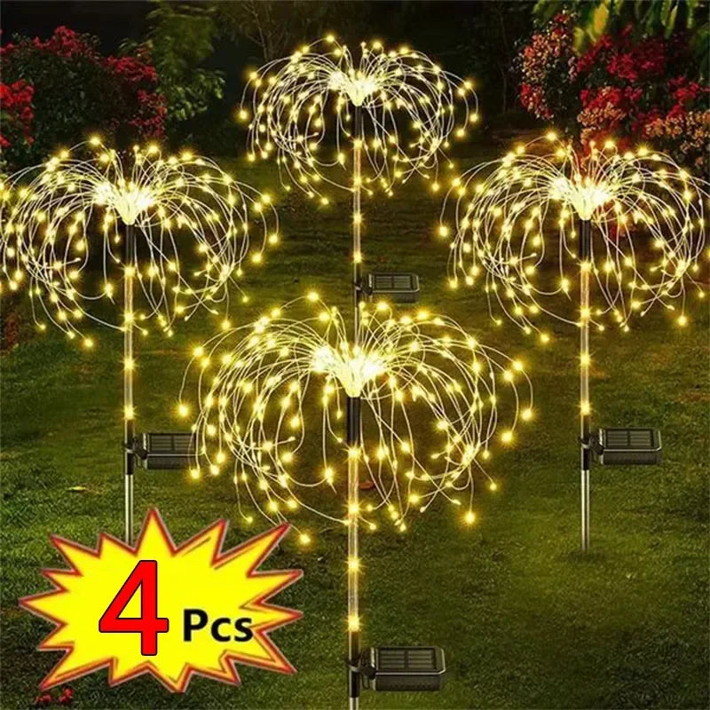 Four solar-powered garden lights shaped like fireworks illuminate a grassy area with warm yellow lights. A "4 Pcs" label is prominent at the bottom corner.