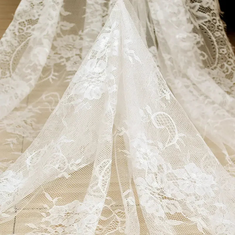 Delicate white lace fabric with intricate floral patterns draped elegantly over a wooden floor, creating a soft and romantic atmosphere.