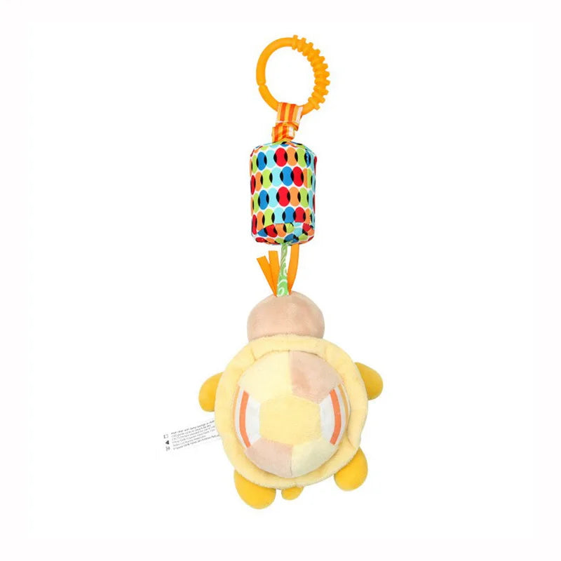 A colorful baby toy features a plush turtle with a yellow shell and dangling orange and green ribbons, attached to a multicolored patterned cylinder and an orange teething ring.