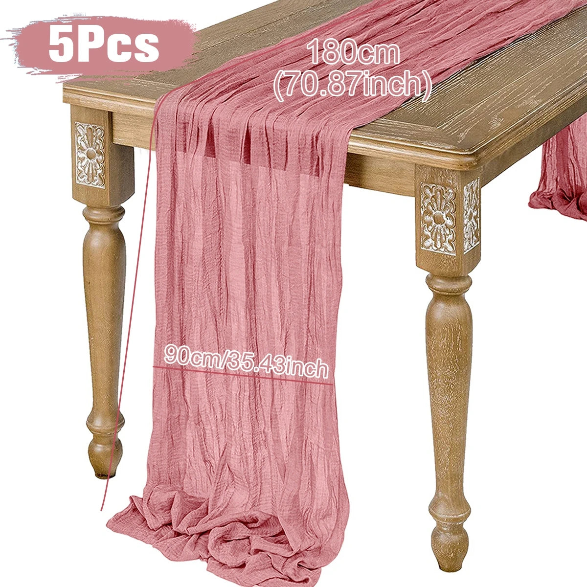 A rustic wooden table adorned with a pink gauze table runner measuring 180 cm by 90 cm. The runner drapes elegantly over the sides, showcasing an intricate floral design on the table legs.