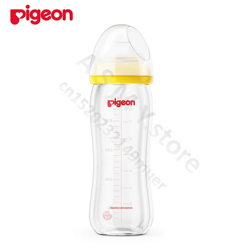 Transparent baby bottle with a yellow cap and measurement markings. The brand "Pigeon" is in red on the bottle. A clear hood covers the nipple. White background.